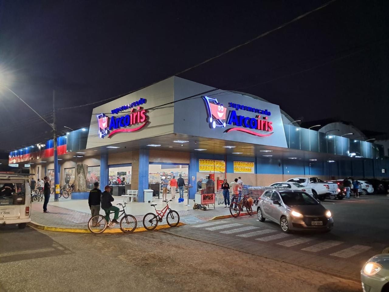 Supermercado Arco-Íris à noite com fachada em ACM e letreiros iluminados