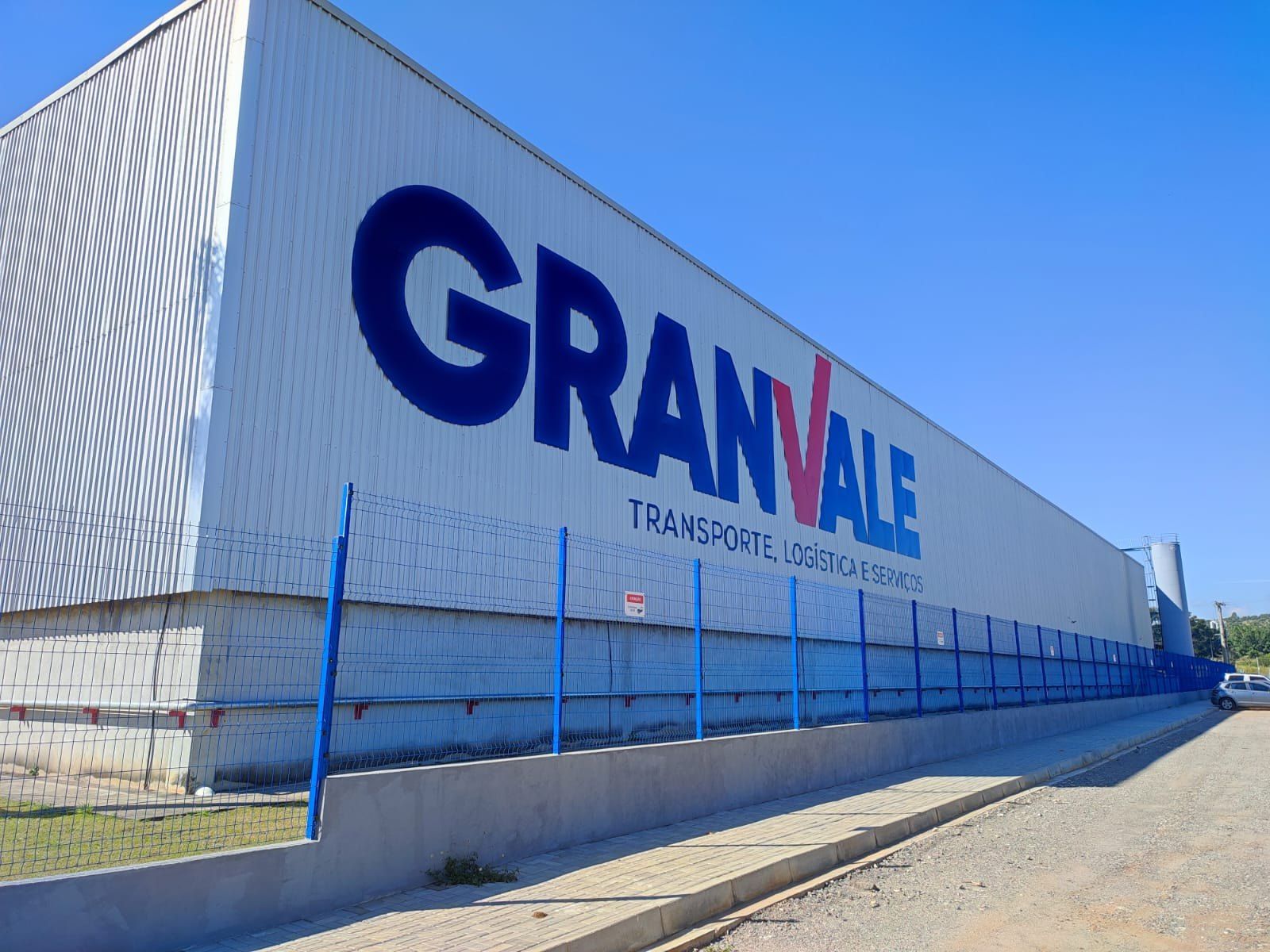 Galpão da Granvale com o logotipo em letras caixa azuis de grande formato, sob céu azul