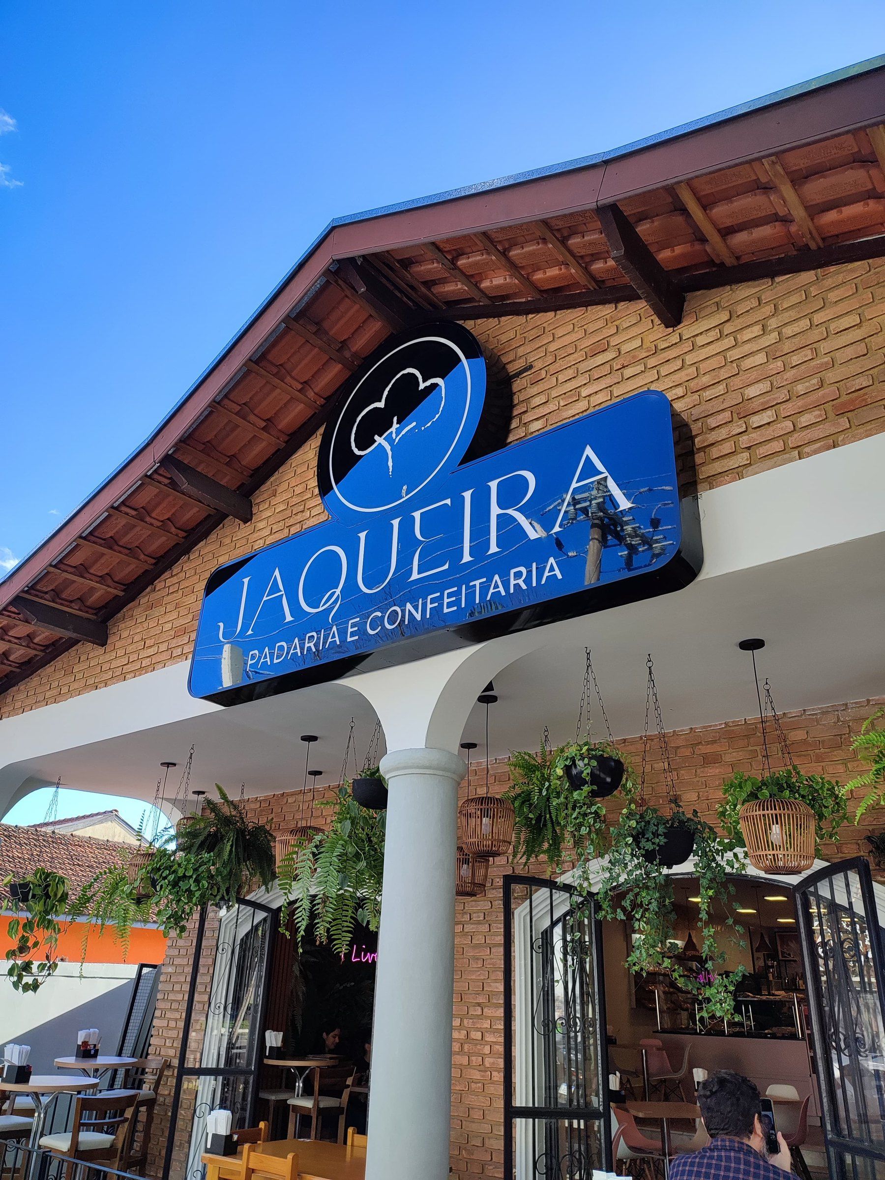 Fachada de tijolos da padaria Jaqueira com letreiro luminoso azul