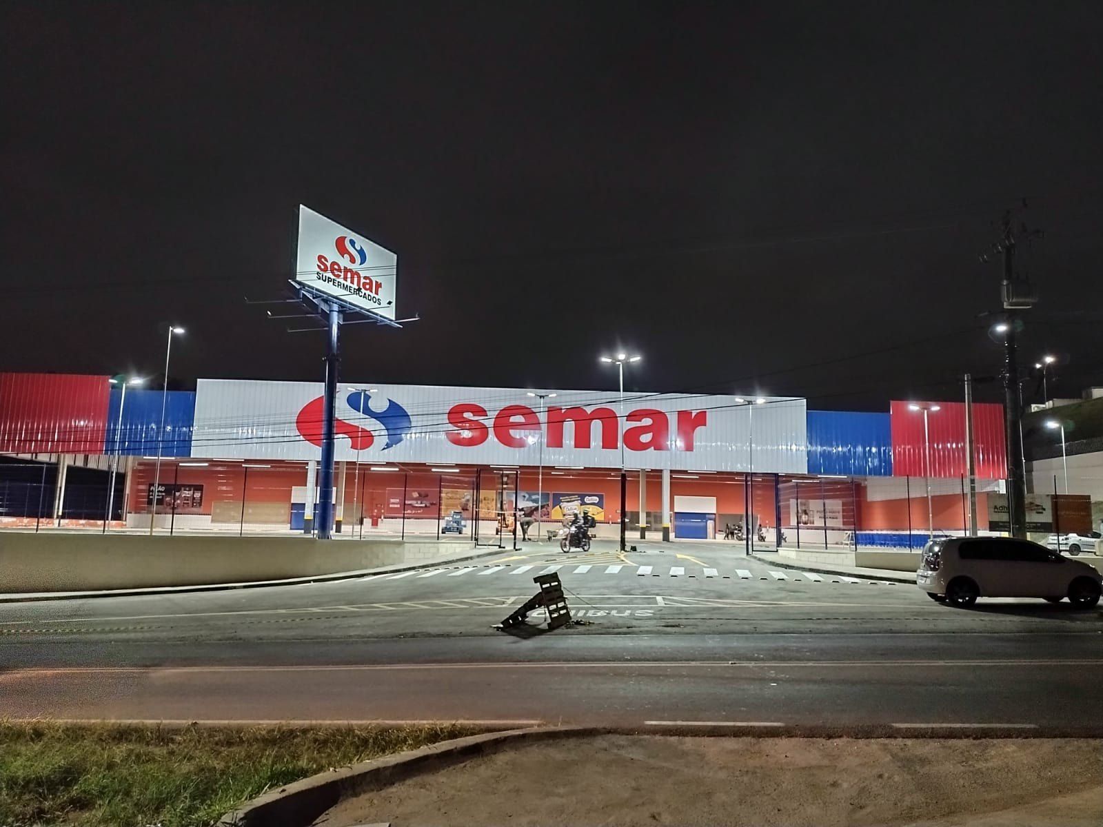 Supermercado Semar à noite com letreiro iluminado na fachada e totem alto