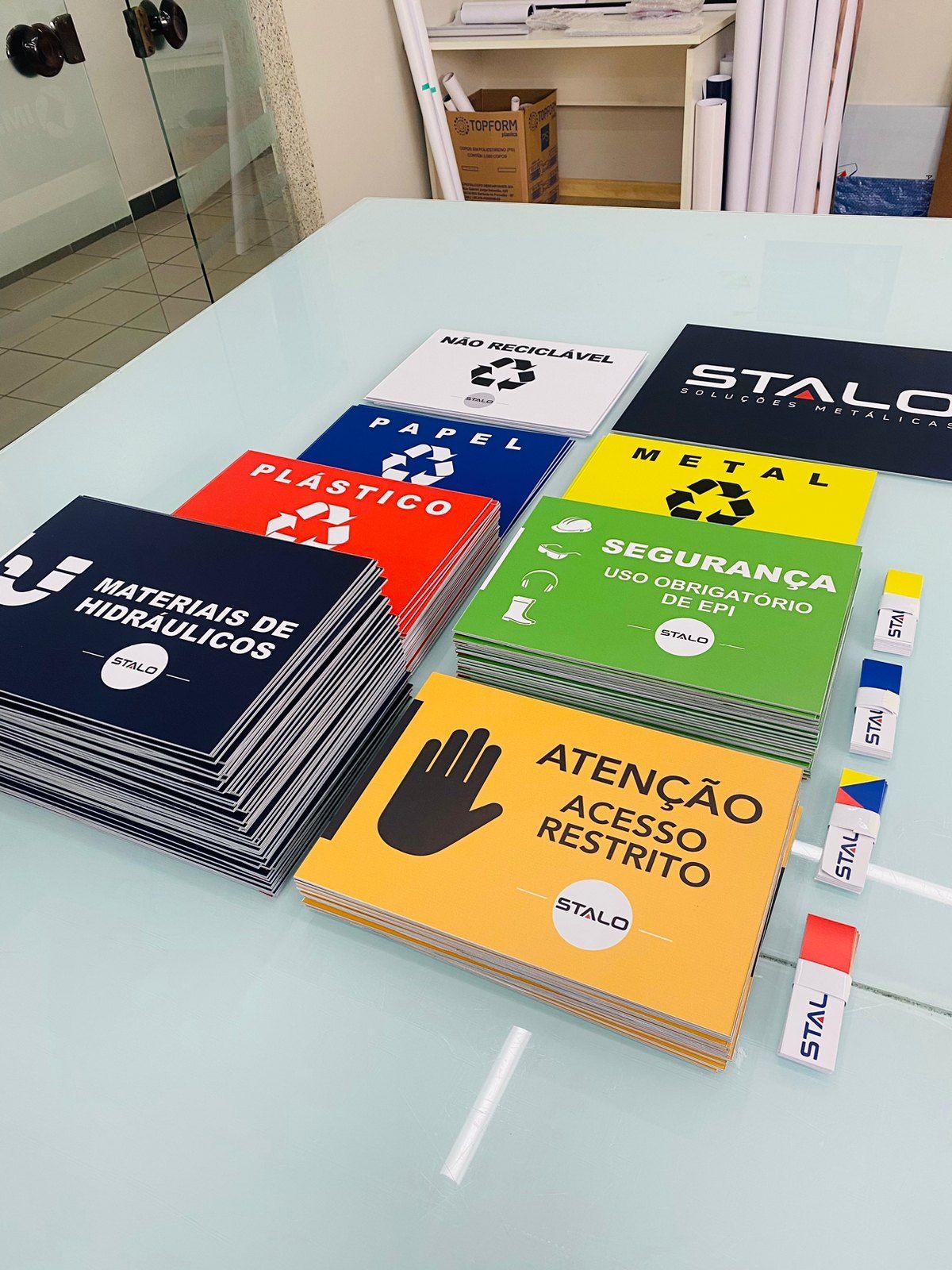 Placas de coleta seletiva e de segurança da Stalo empilhadas sobre a mesa